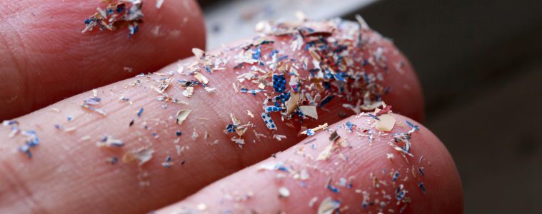 Tiny rainbow microplastic pieces on three fingers