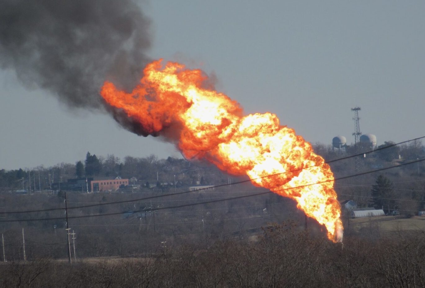 A massive tower of flames with black smoke as seen from afar