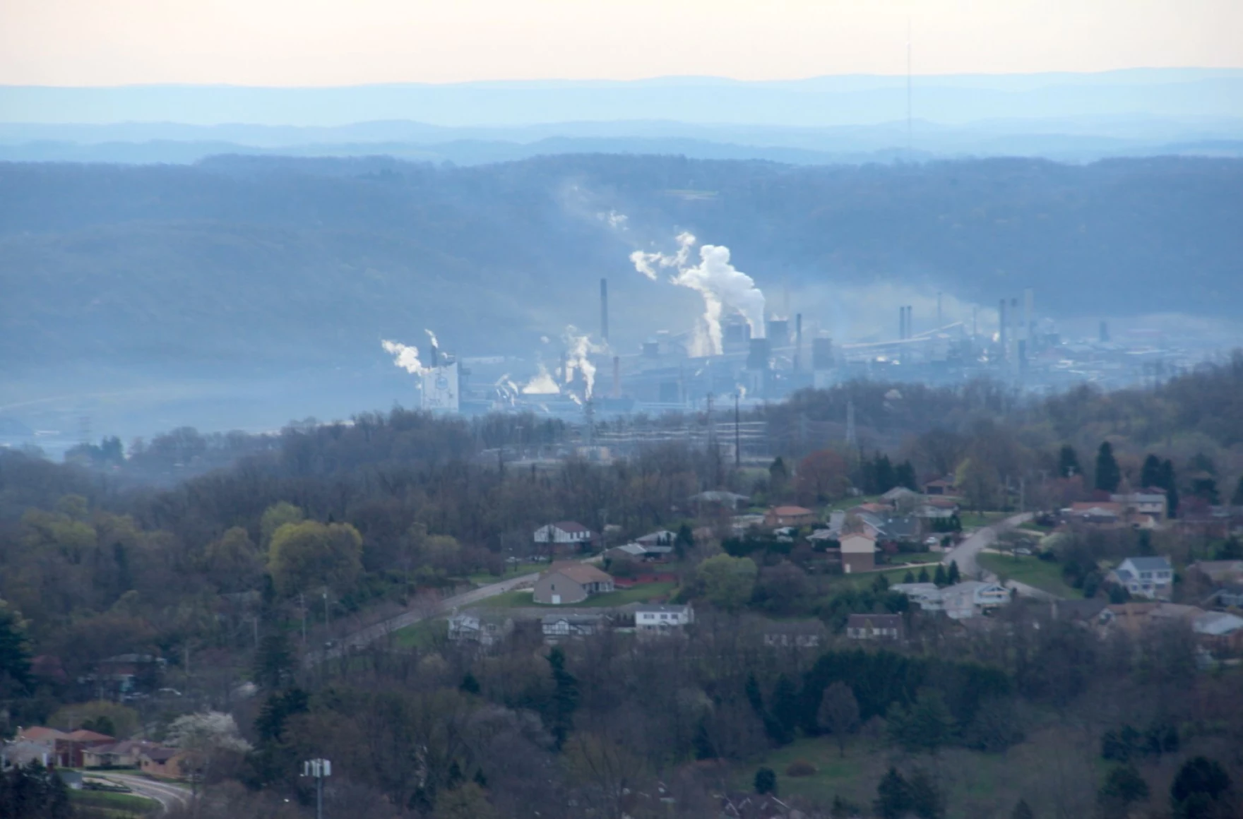 landscape shot of emissions rising from smoke stakes in the distance over a valley