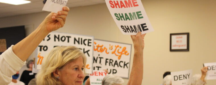 Woman holding a sign that says "SHAME, SHAME, SHAME" among other signs