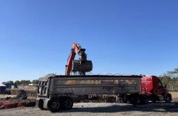 a front loader is dumping soil into a large tractor trailer truck in the foreground.