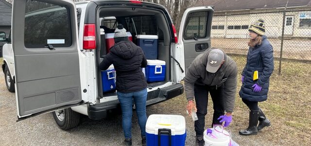 Three people unload blue coolers from a van