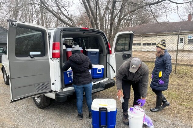 Three people unload blue coolers from a van