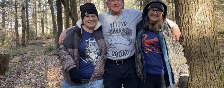 Three people stand arm-and-arm in a forest.