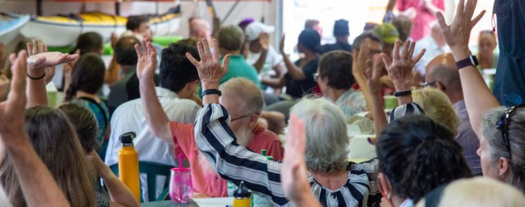 People are seated at tables, some with their hands raised.