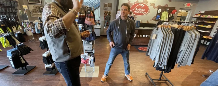 Two men stand inside a store with clothing and other outdoor gear.