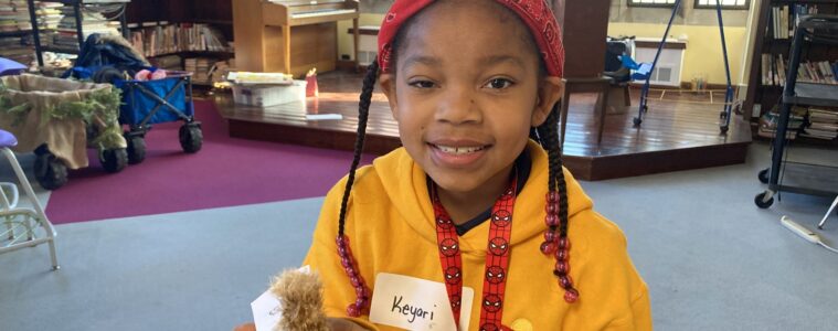 A young girl in a yellow sweatshirt holds a museum specimen of a great horned owl in the pal of her hand.