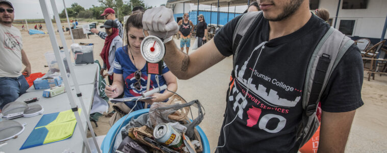 A man holds a blue bucket filled with cans, bottle and other trash picked up at beach clean up.