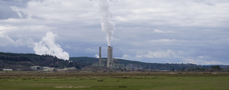 A power plant with large smokestacks shown from a distance.