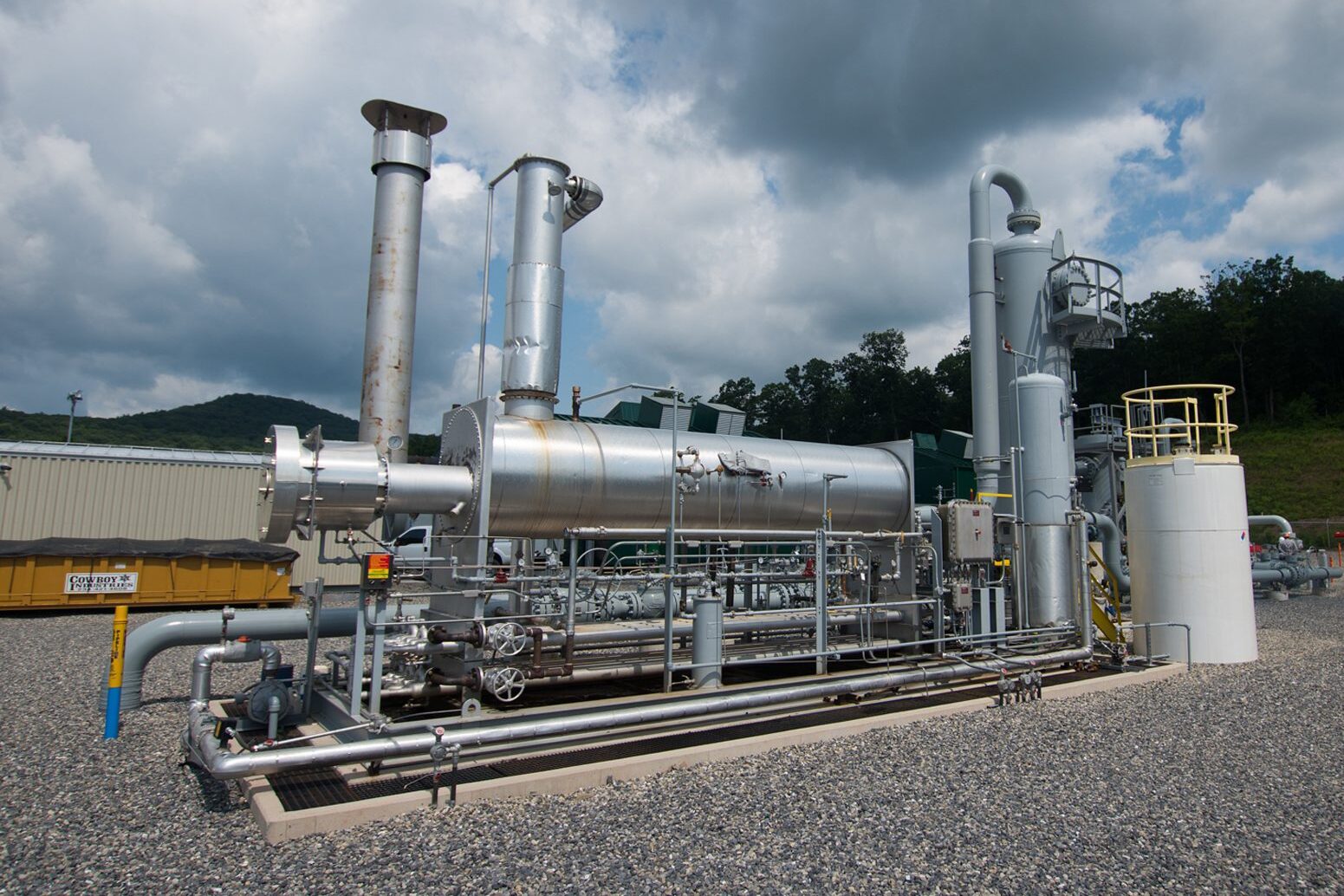A shiny silver gas processing unit against a blue sky with white clouds.
