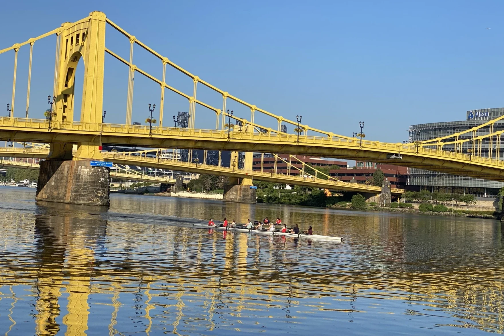 Rowers in a river underneath a yellow bridge.