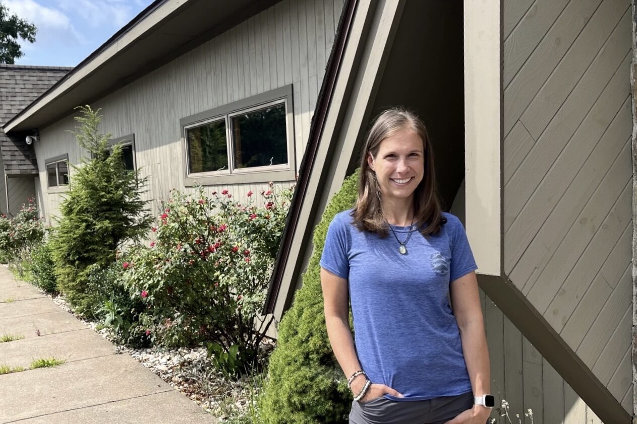 A woman in blue t-shirt and shorts stands in front of a building.