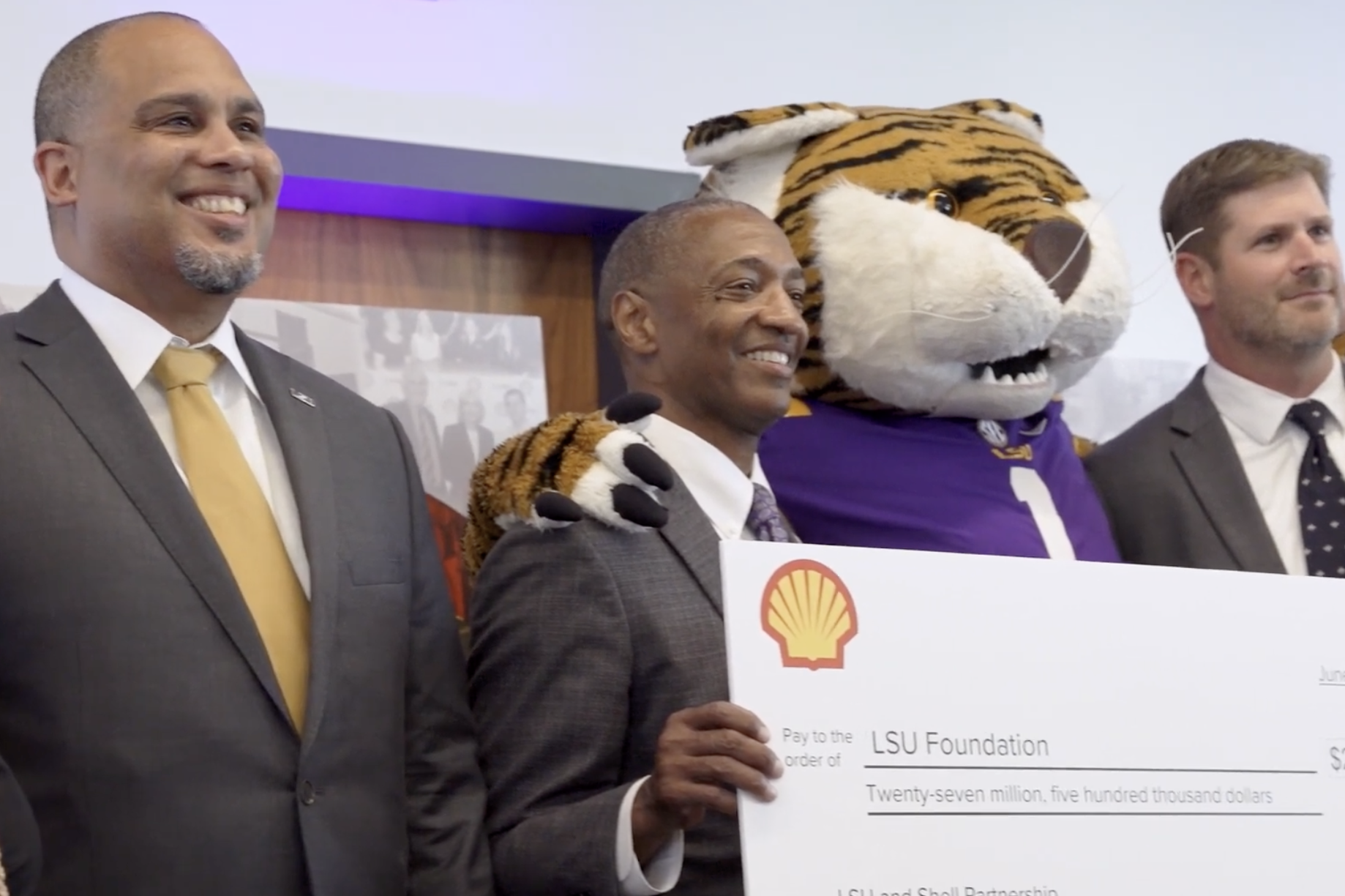 Three men and a woman stand behind a sign that is a large check.