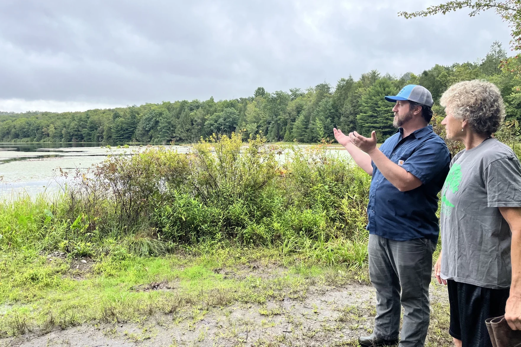 A man and a woman stand near the a lake under a cloudy sky.