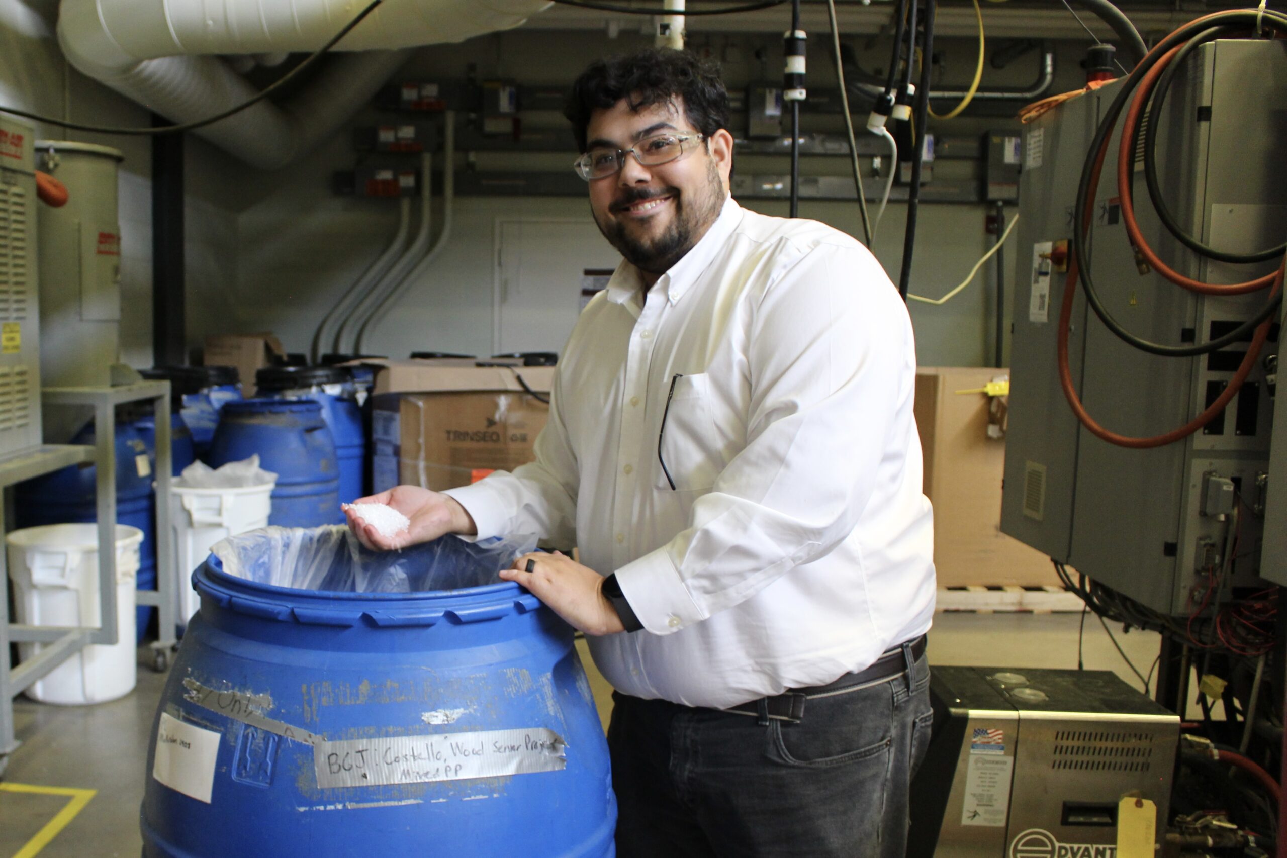 A man stands with his hand in a barrel filled with tiny white plastic pellets