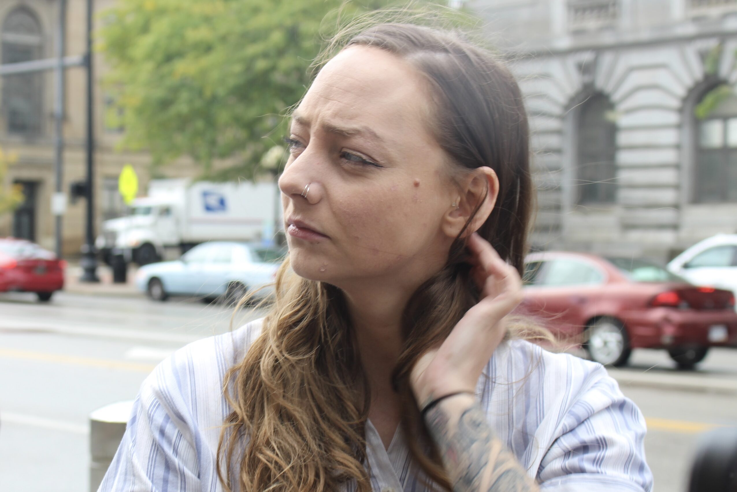 A woman with long brown hair tucks a strand behind her ear.