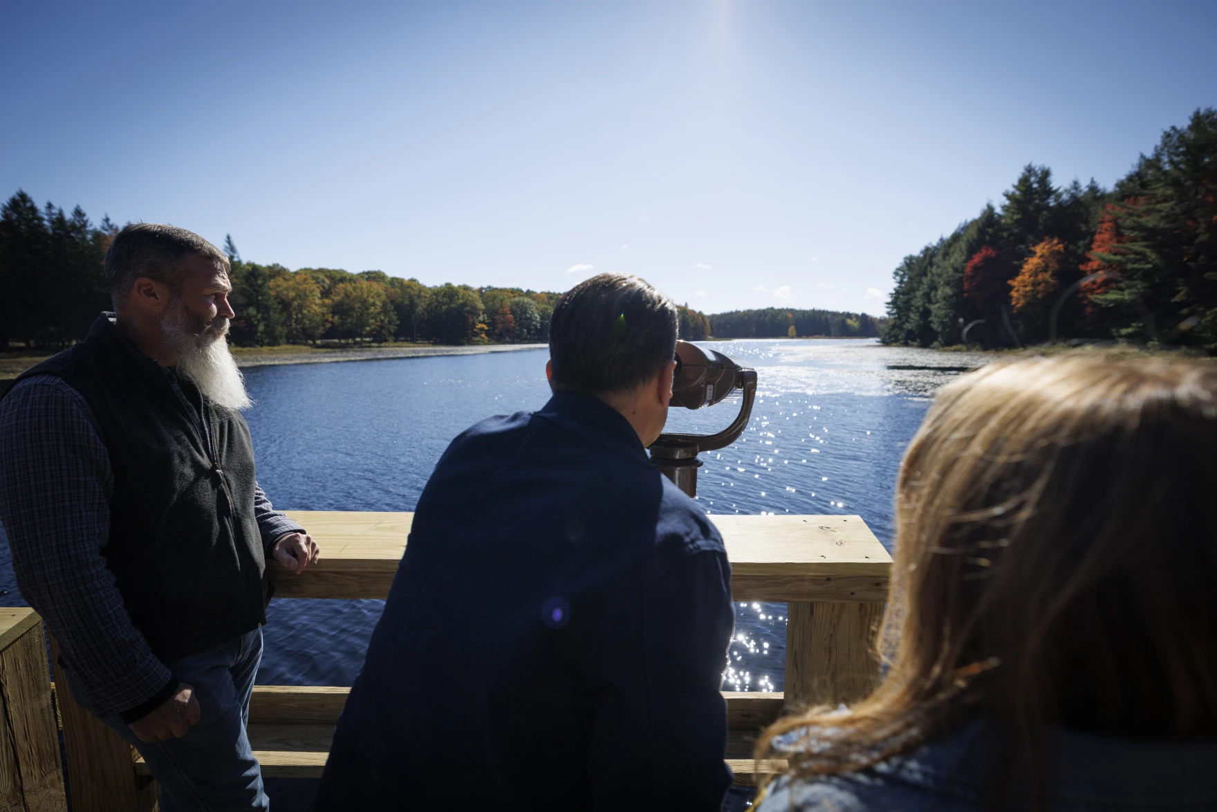 A person looks through a viewfinder overlooking a lake.