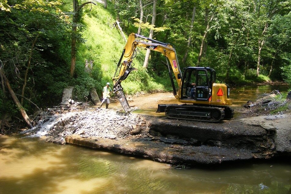 An excavator on a dam along a small creek