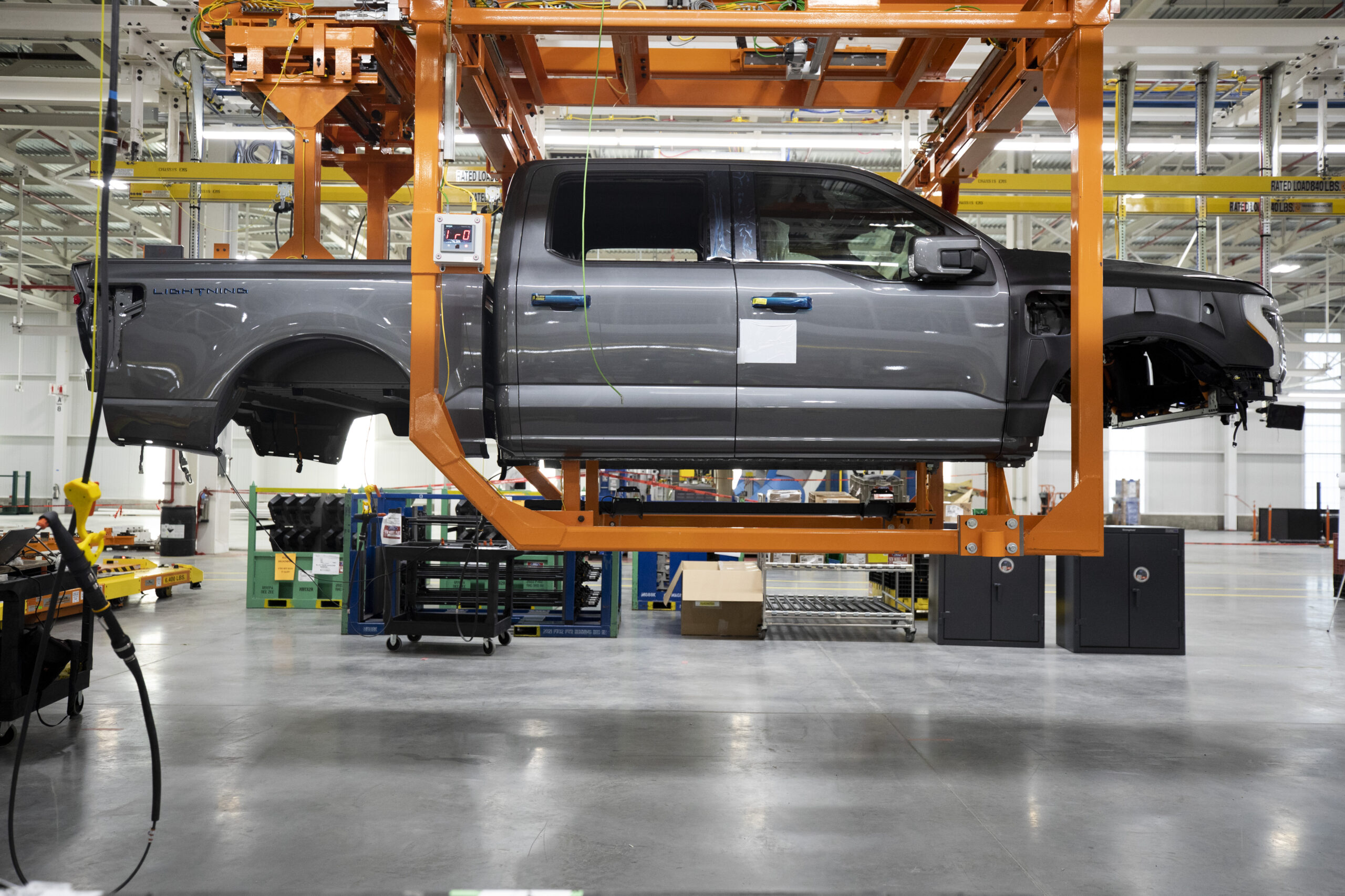 The body of a gray pick-up truck suspended in the air in a factory.