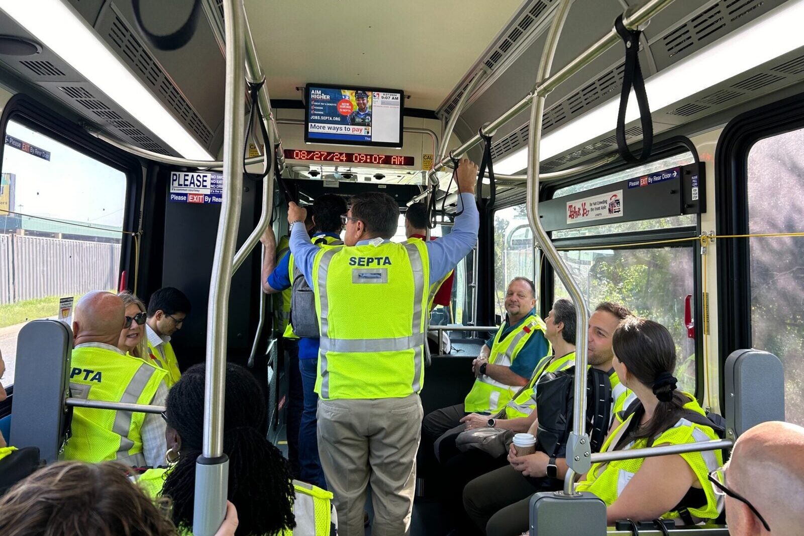 Transit workers wearing bright yellow safety vests ride in a bus.