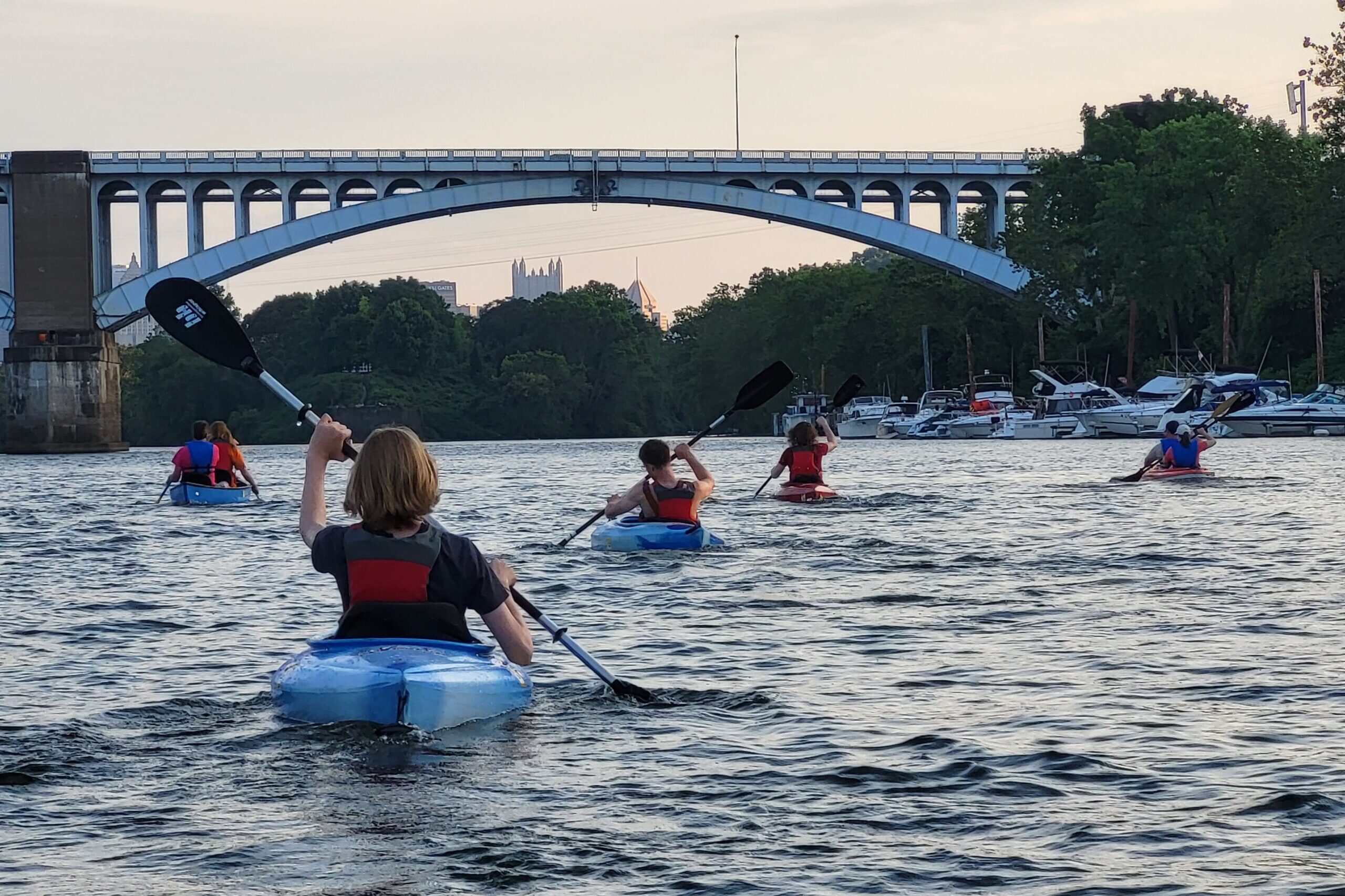 kayaks from behind heading toward bridge with Pittsburgh in background