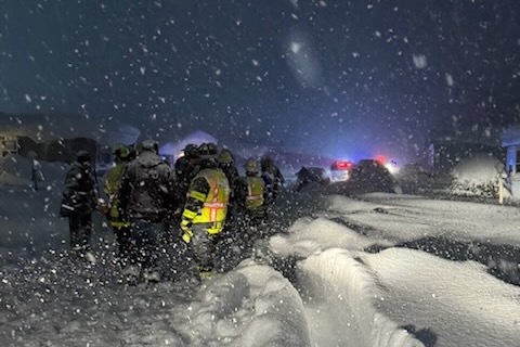 A man in a yellow florescent vest, seen from the back, standing by large piles of snow