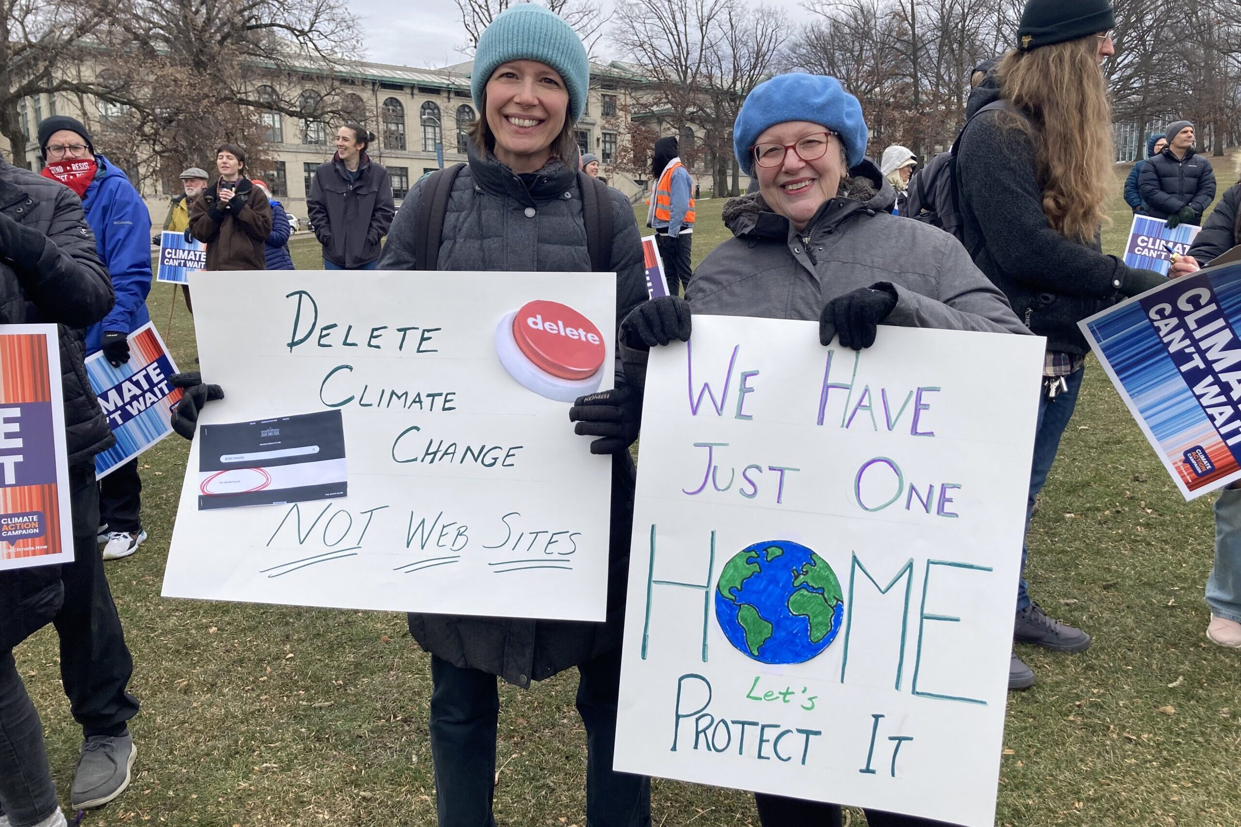 Two women in blue hats stand in a crowd with climate protest signs