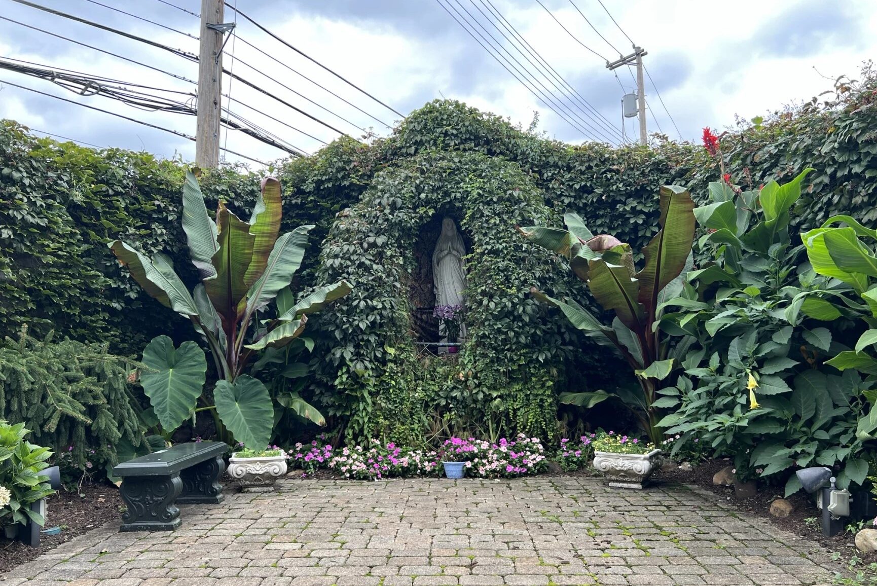 A stone altar with a Mary statue is surrounded by green leafy plants