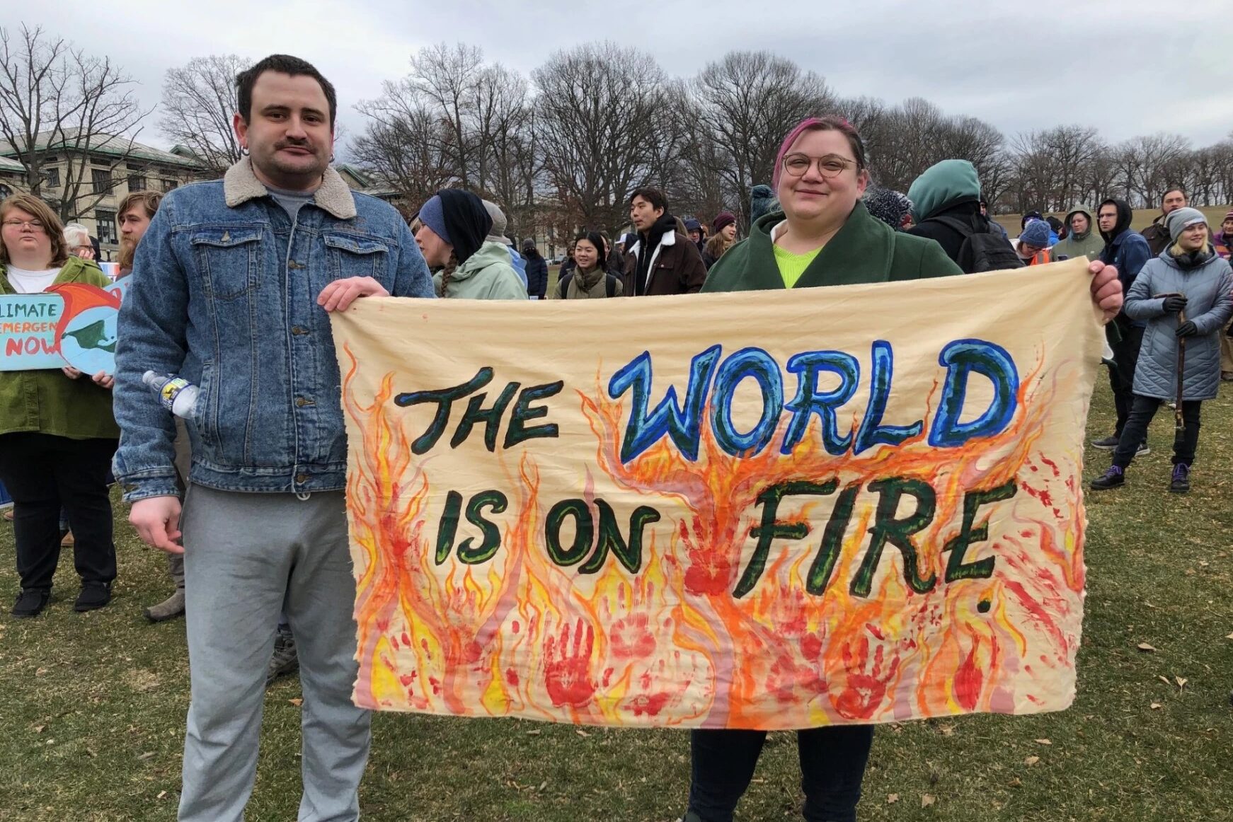 A man and a woman hold the corners of an orange banner at a climate rally