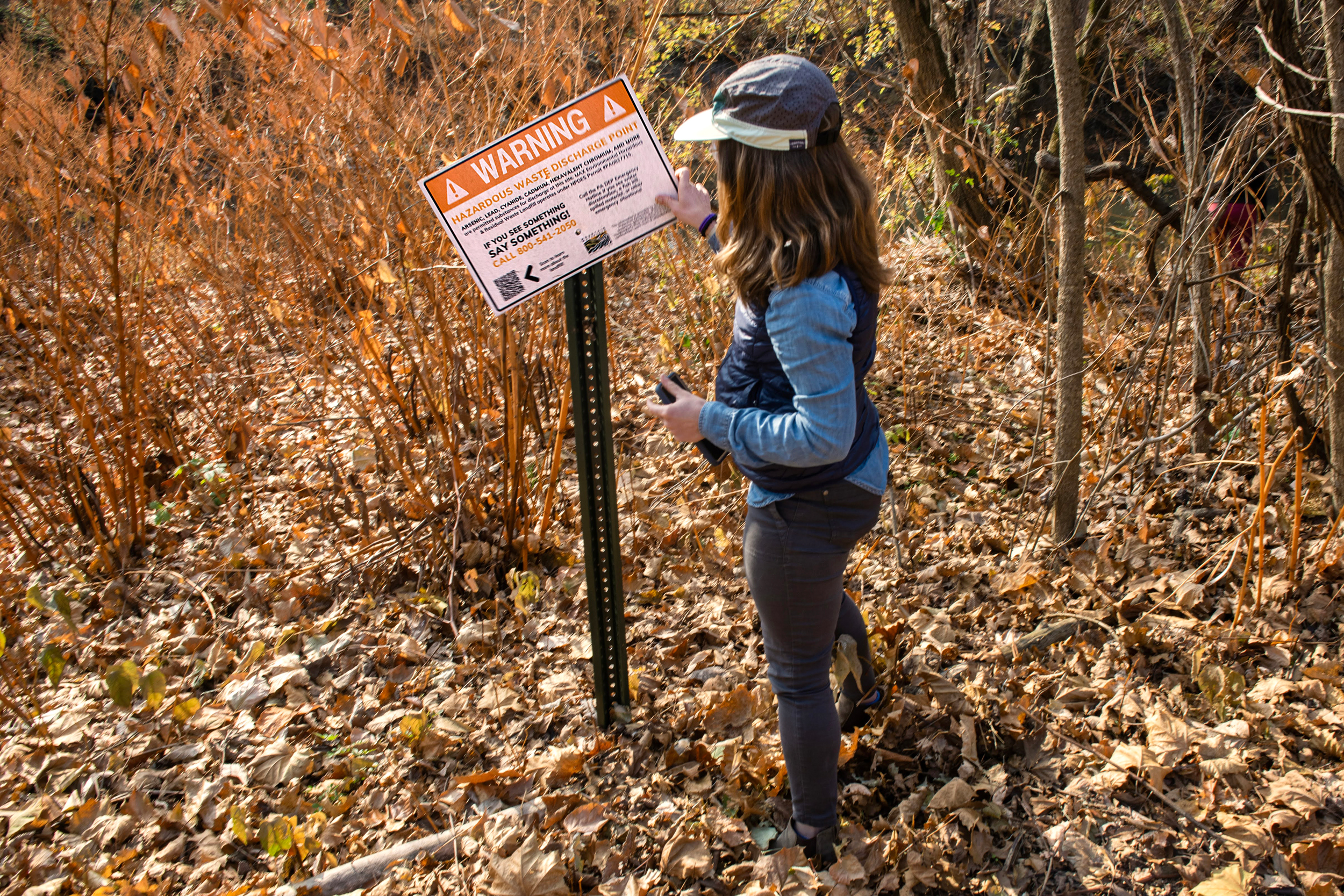 A woman adjusts a sign posted in the woods.