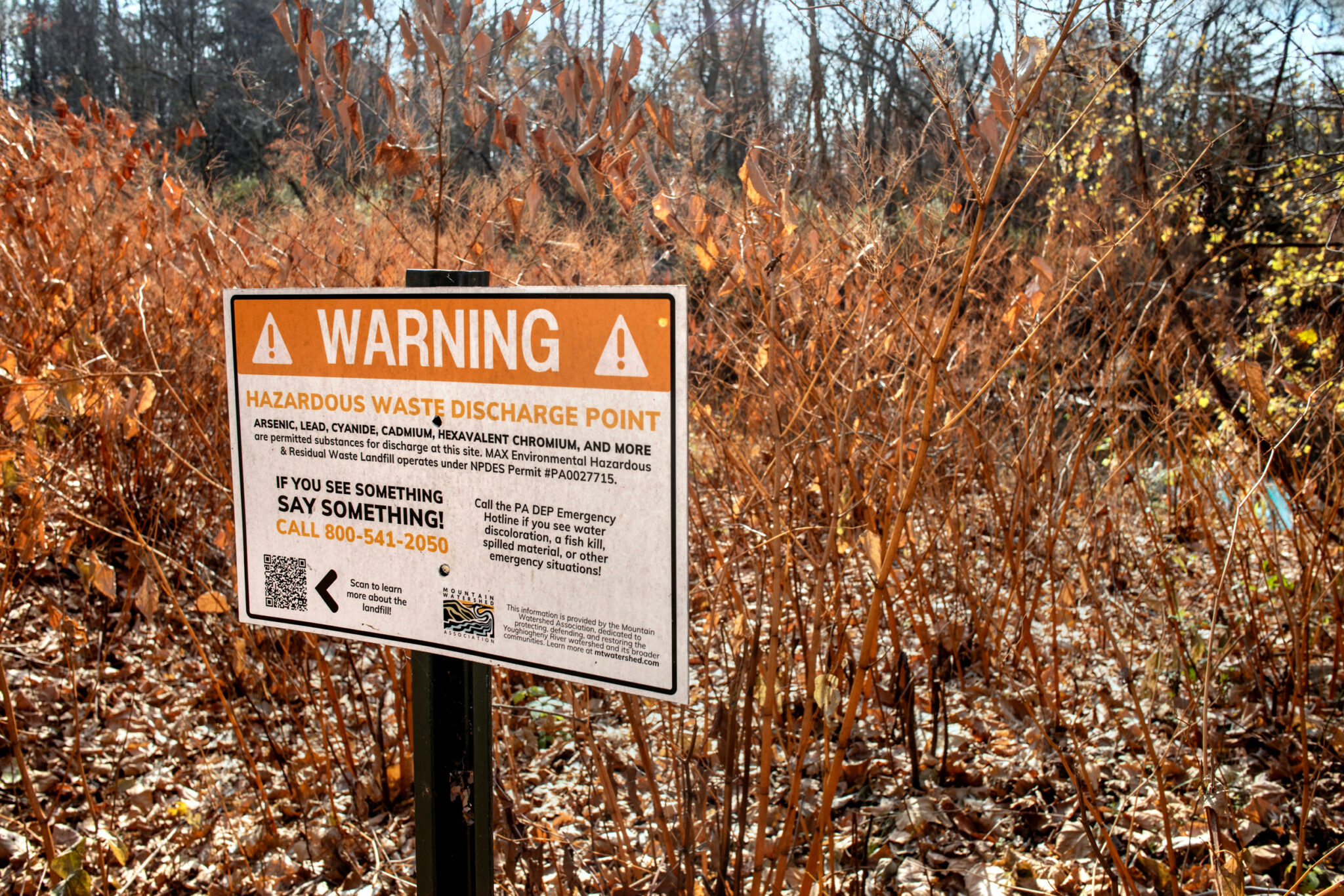 A warning sign posted in a wooded area reading, "WARNING Hazardous Waste Discharge Point."