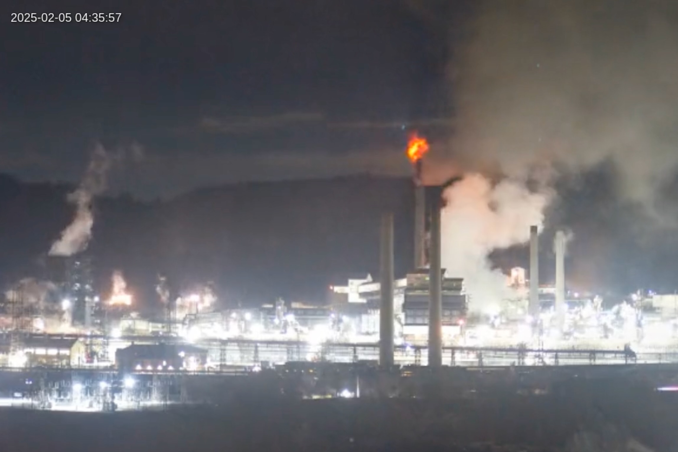 A view of a large industrial facility with a ball of fire coming out of a smokestack.