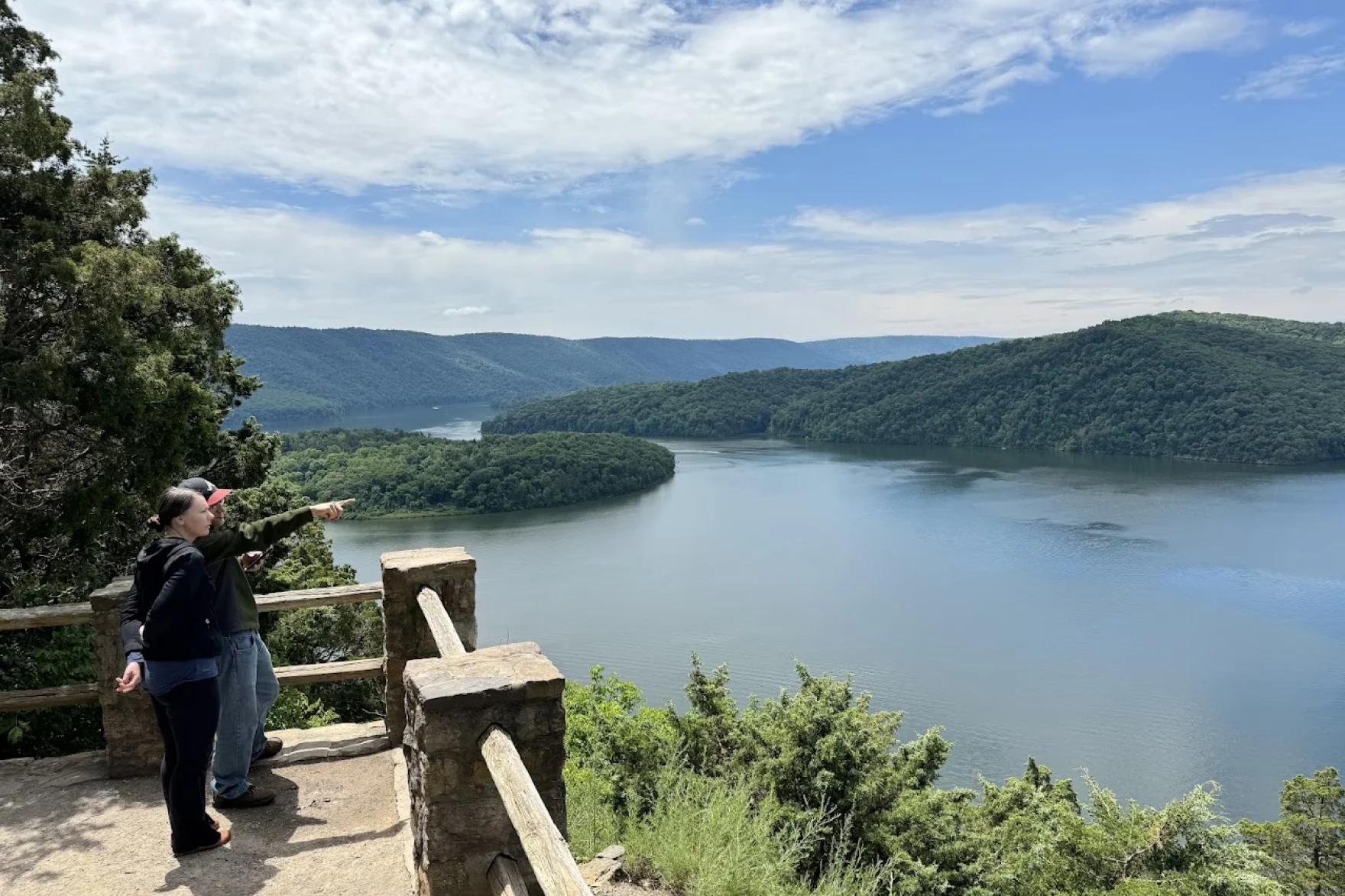 Two people stand at an observation deck overlooking a large lake